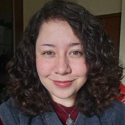 Retrato de uma mulher com cabelo cacheado e sorriso, em um ambiente interno.